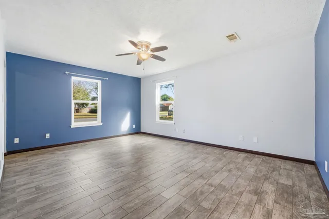 an empty room with wooden floor chandelier fan and windows