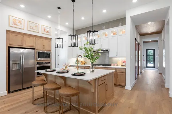 a kitchen with stainless steel appliances granite countertop a refrigerator a sink a stove a kitchen island and chairs with wooden floor