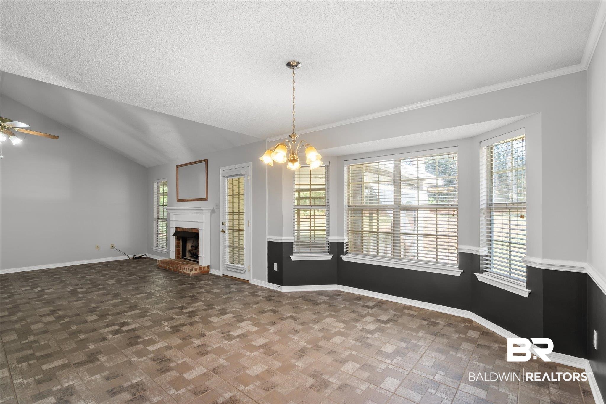 7410 East Lakeview Drive Mobile, AL 36695 - Photo 6 of 20 Unfurnished dining area featuring ceiling fan with notable chandelier, vaulted ceiling, a brick fireplace, ornamental molding, and a textured ceiling