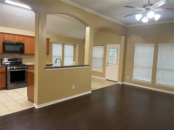an empty room with wooden floor a kitchen view and a windows