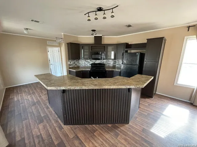 a living room with stainless steel appliances kitchen island granite countertop a refrigerator a sink dishwasher a dining table and chairs with wooden floor