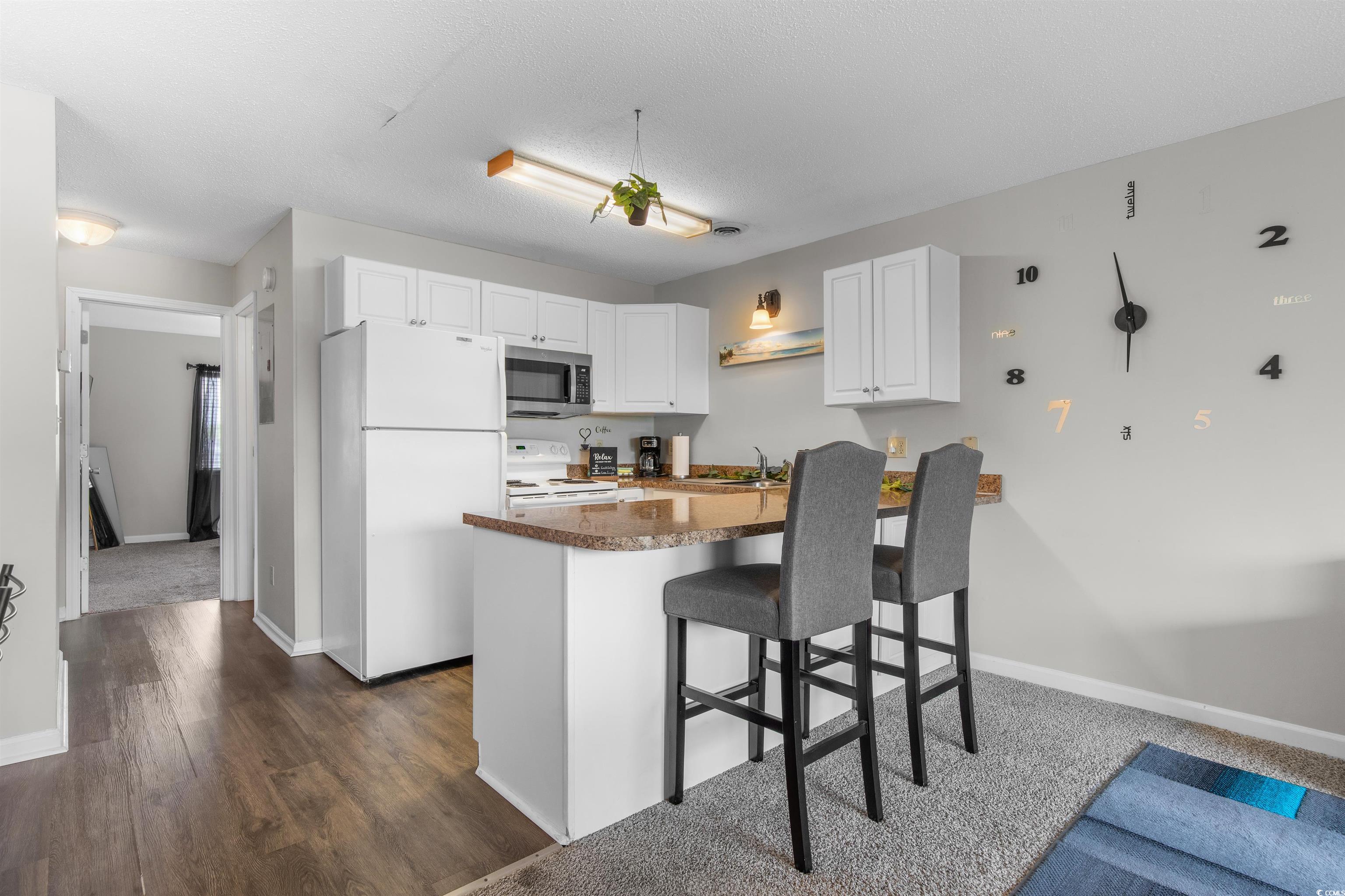 1850 Colony Drive, Unit 3D Surfside Beach, SC 29575 - Photo 15 of 38 Kitchen featuring white appliances, a kitchen bar, white cabinetry, a peninsula, and dark wood-style floors