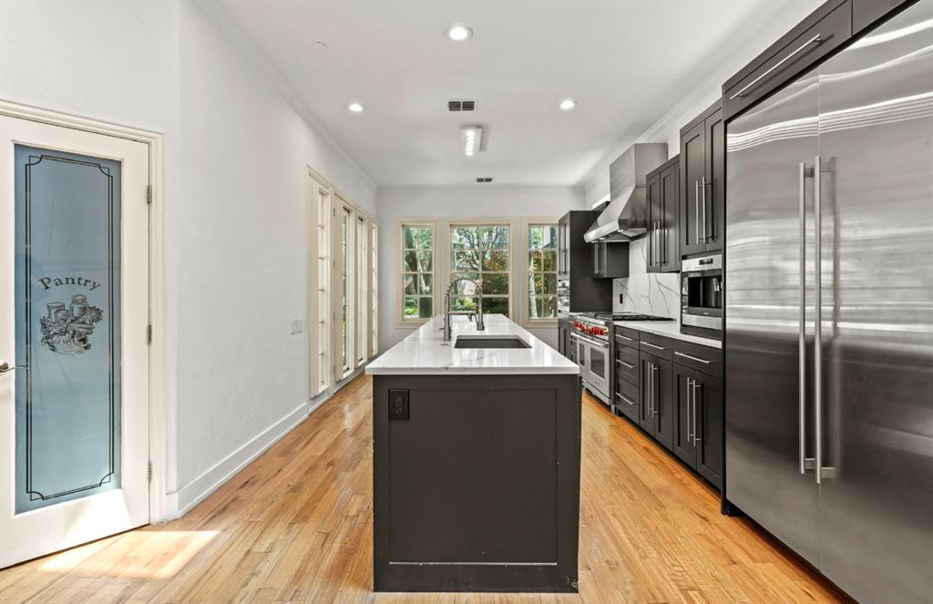11911 Edgestone Road Dallas, TX 75230 - Photo 7 of 40 Kitchen featuring premium appliances, an island with sink, light wood finished floors, wall chimney exhaust hood, and recessed lighting