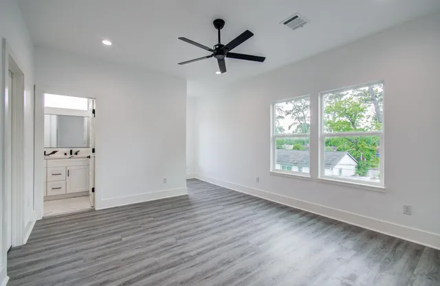 an empty room with wooden floor a ceiling fan and windows
