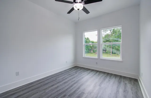 an empty room with wooden floor chandelier fan and windows