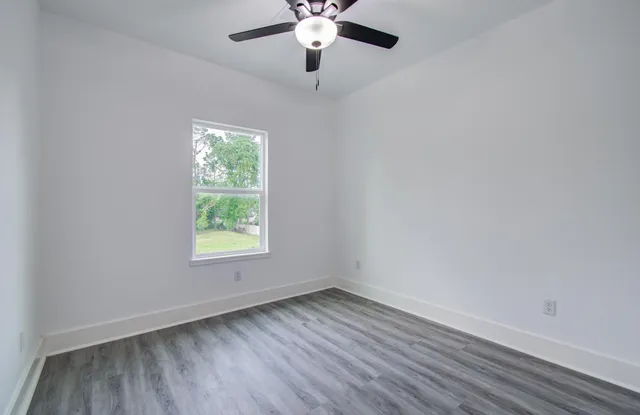 an empty room with wooden floor chandelier fan and windows