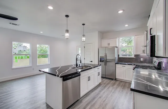 a kitchen with stainless steel appliances granite countertop hardwood floor sink stove large window and cabinets