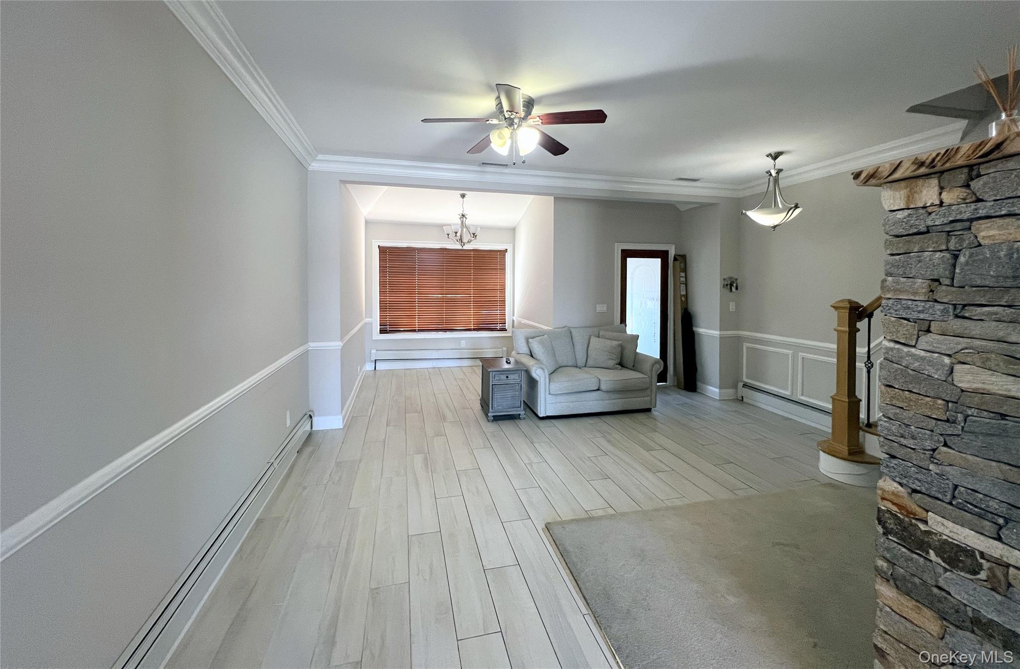 67-31 52nd Road Queens, NY 11378 - Photo 3 of 21 Living area featuring light wood finished floors, crown molding, baseboard heating, ceiling fan, and a chandelier