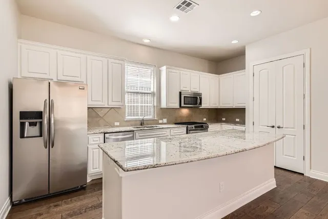 a kitchen with stainless steel appliances granite countertop a refrigerator a stove a sink and white cabinets