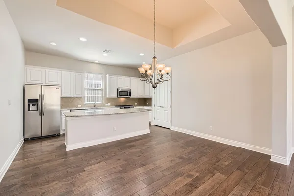 a large kitchen with granite countertop a white cabinets stainless steel appliances and a chandelier