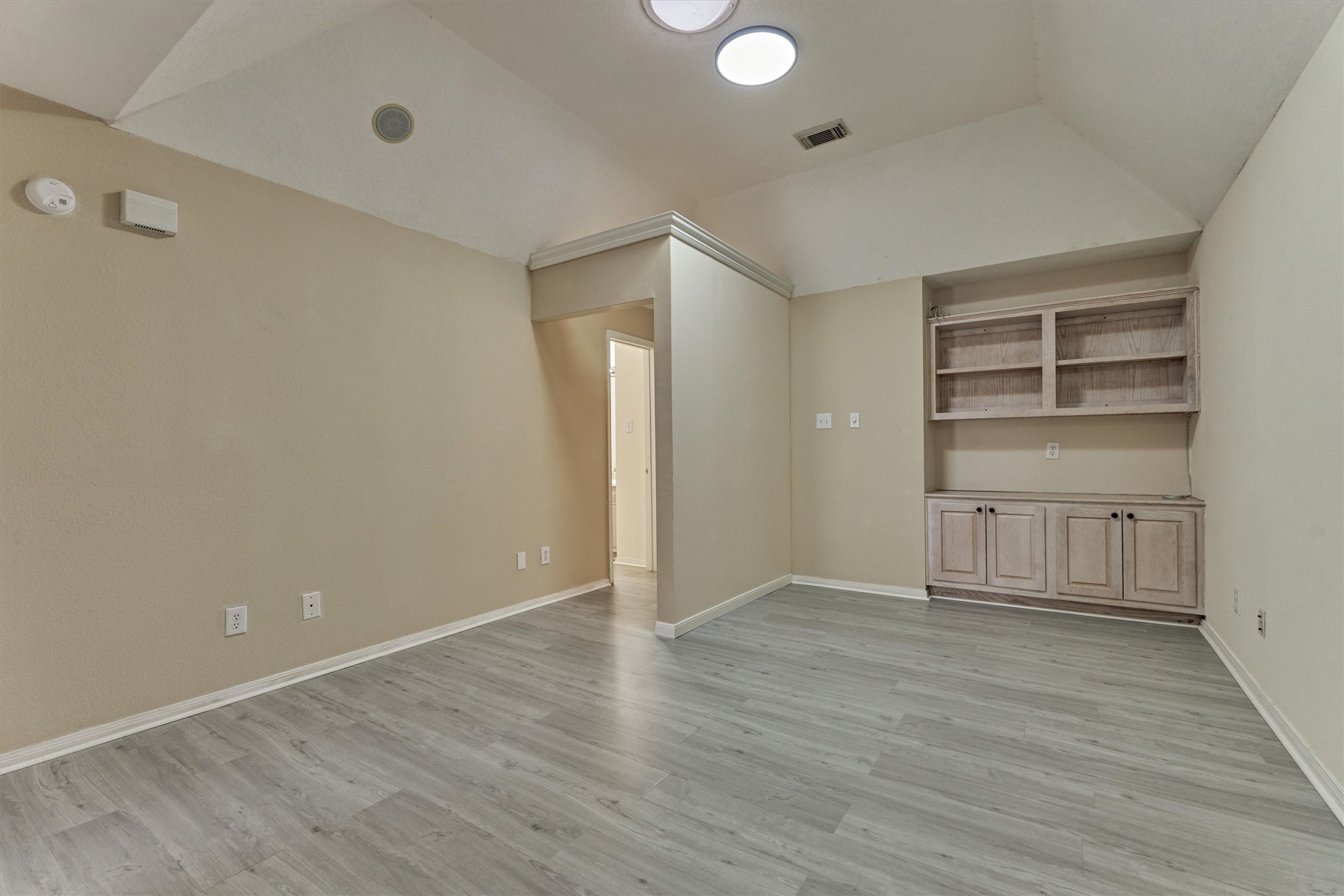 14420 Walters Road, Unit 26 Houston, TX 77014 - Photo 24 of 45 This photo showcases the upstairs game room or office space with high ceilings, a skylight, and wood-look flooring. It features built-in shelving, providing ample storage space. An adjacent hallway leads to additional bedrooms, and large windows allow natural light to fill the space.