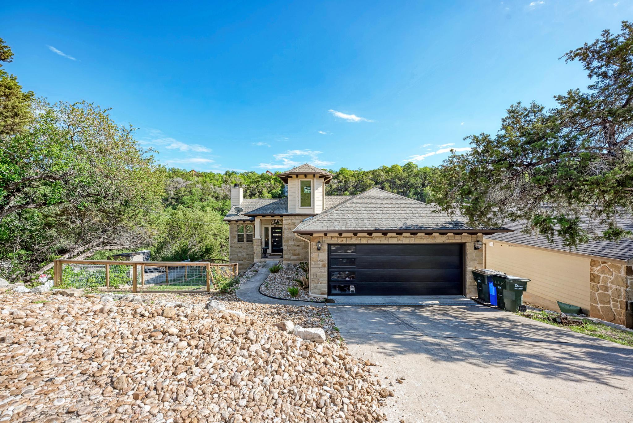 2605 Indian Creek Road Austin, TX 78734 - Photo 1 of 33 Stone facade residence featuring a prominent two-car garage with frosted glass panels, a paved driveway, and an elevated entryway