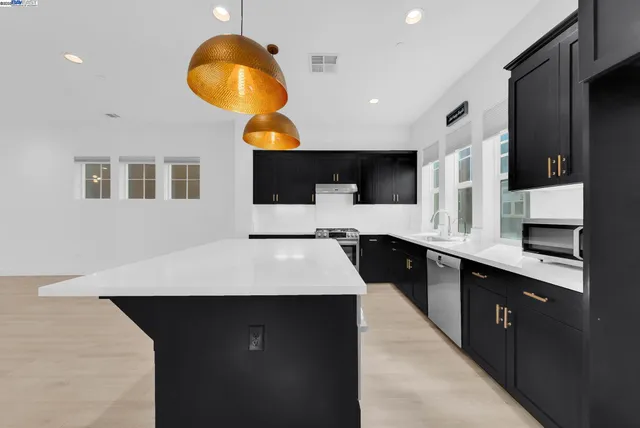 a large kitchen with stainless steel appliances kitchen island granite countertop a sink dishwasher and a black stove next to a window