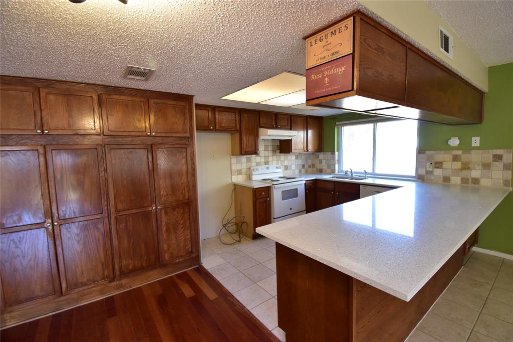 5414 Castleview Lane Garland, TX 75044 - Photo 7 of 20 Kitchen featuring a peninsula, white electric range oven, a textured ceiling, tasteful backsplash, and light tile patterned floors