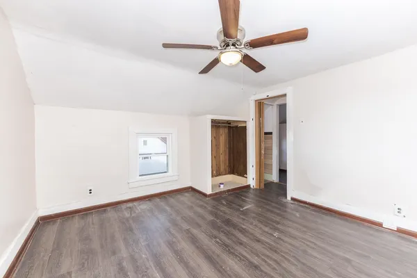 a view of an empty room with wooden floor and a ceiling fan