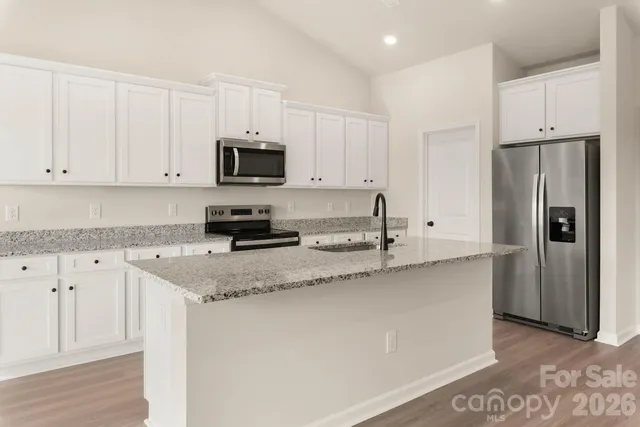 a kitchen with stainless steel appliances granite countertop a refrigerator a stove a sink and white cabinets