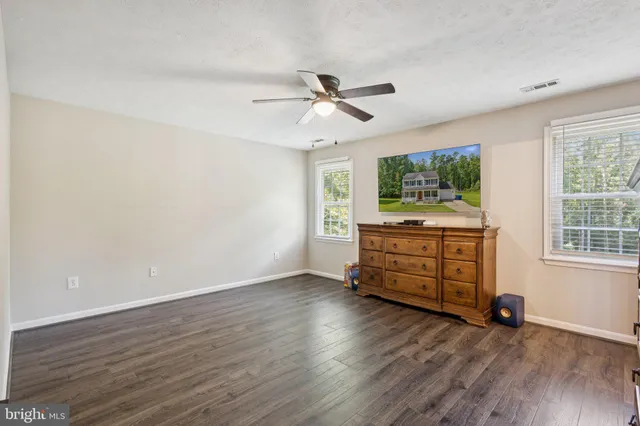 an empty room with wooden floor fan and windows