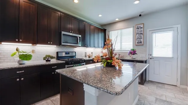 a kitchen with kitchen island granite countertop wooden cabinets a sink dishwasher and a stove with wooden floor