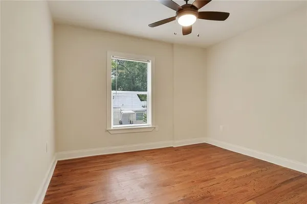 an empty room with wooden floor chandelier fan and windows