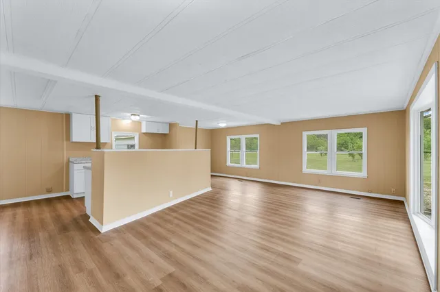 a view of a kitchen and an empty room with wooden floor and a window