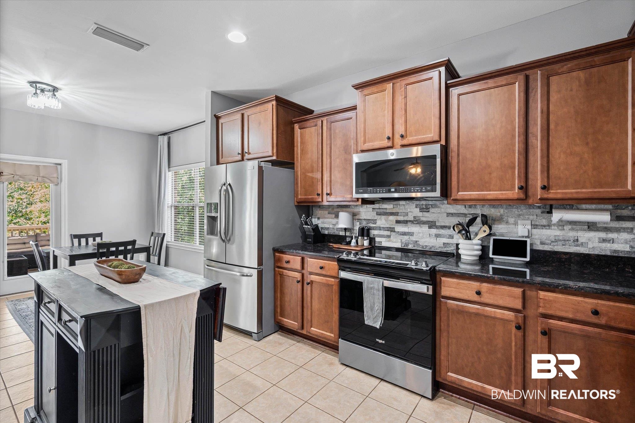 3739 Whitestone Drive Semmes, AL 36575 - Photo 8 of 25 Spacious kitchen featuring warm wood cabinetry, dark countertops, tile flooring, and a decorative tile backsplash