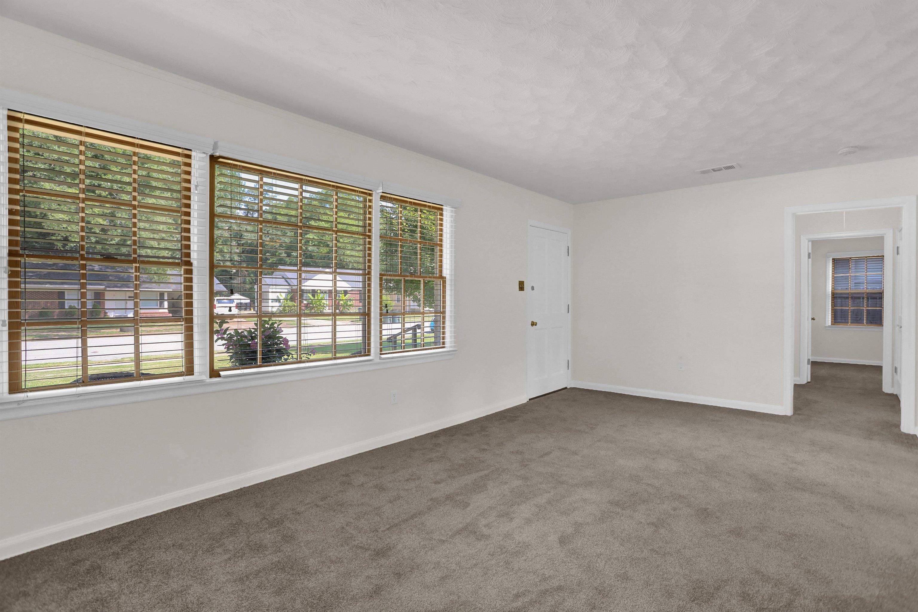 4545 Flamingo Road Memphis, TN 38117 - Photo 9 of 34 Spacious living area featuring three large windows with wood-finish blinds, light-colored walls, and neutral carpet flooring
