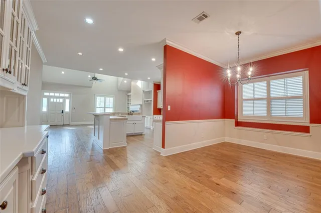 a view of an empty room and kitchen with wooden floor