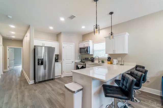 a kitchen with stainless steel appliances granite countertop a refrigerator a sink dishwasher a stove and white cabinets with wooden floor