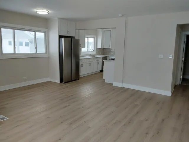an empty room with wooden floor and a kitchen