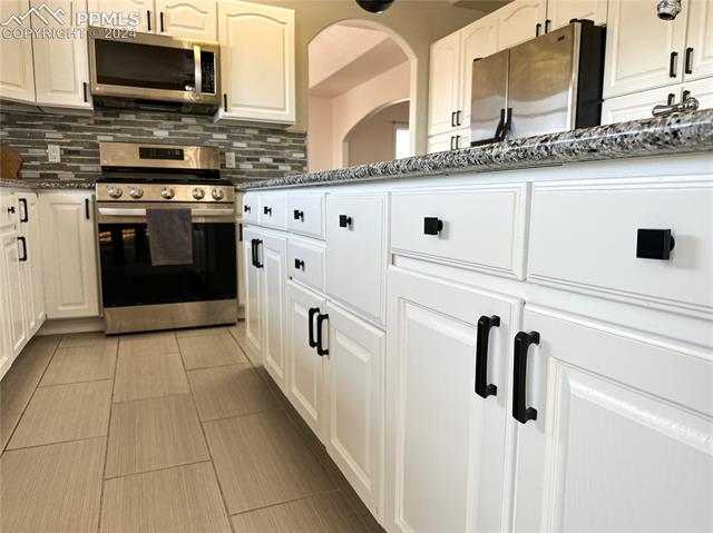 11125 Eureka Road Calhan, CO 80808 - Photo 10 of 44 Kitchen featuring tasteful backsplash, dark stone countertops, white cabinets, light tile floors, and appliances with stainless steel finishes