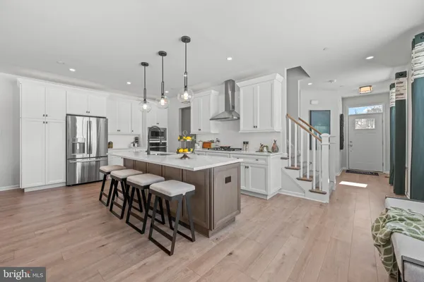 a kitchen with stainless steel appliances kitchen island granite countertop a refrigerator a stove a sink and white cabinets with wooden floor