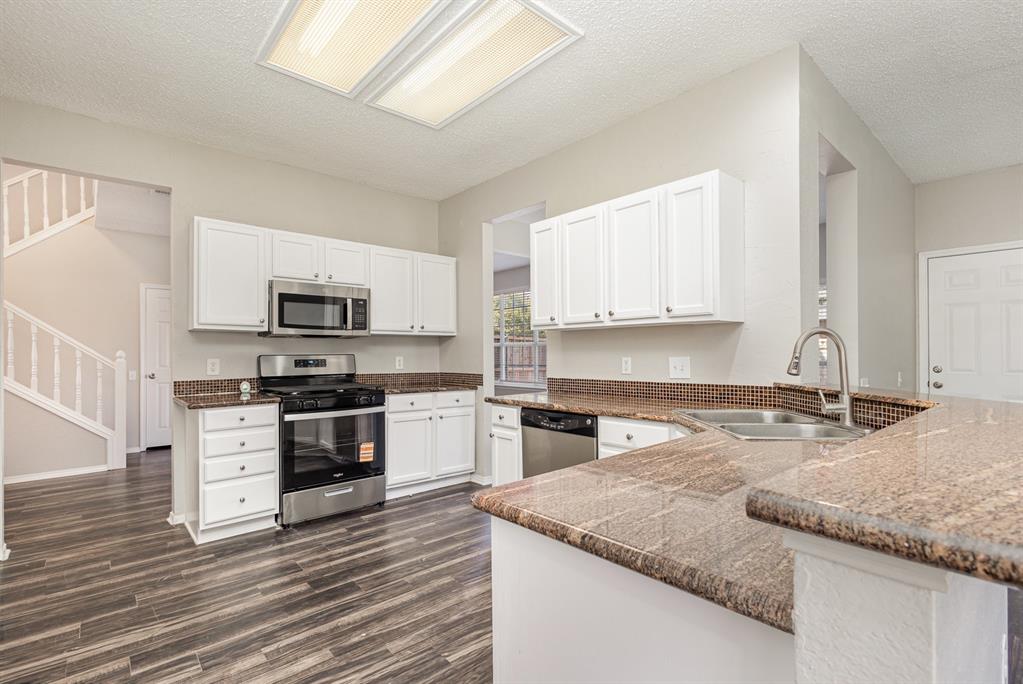 7100 Layla Road Arlington, TX 76016 - Photo 7 of 19 Kitchen with a textured ceiling, appliances with stainless steel finishes, white cabinetry, a peninsula, and dark stone counters