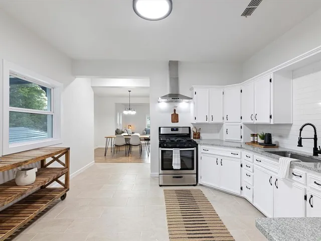 a kitchen with stainless steel appliances granite countertop a stove a sink dishwasher and white cabinets with wooden floor