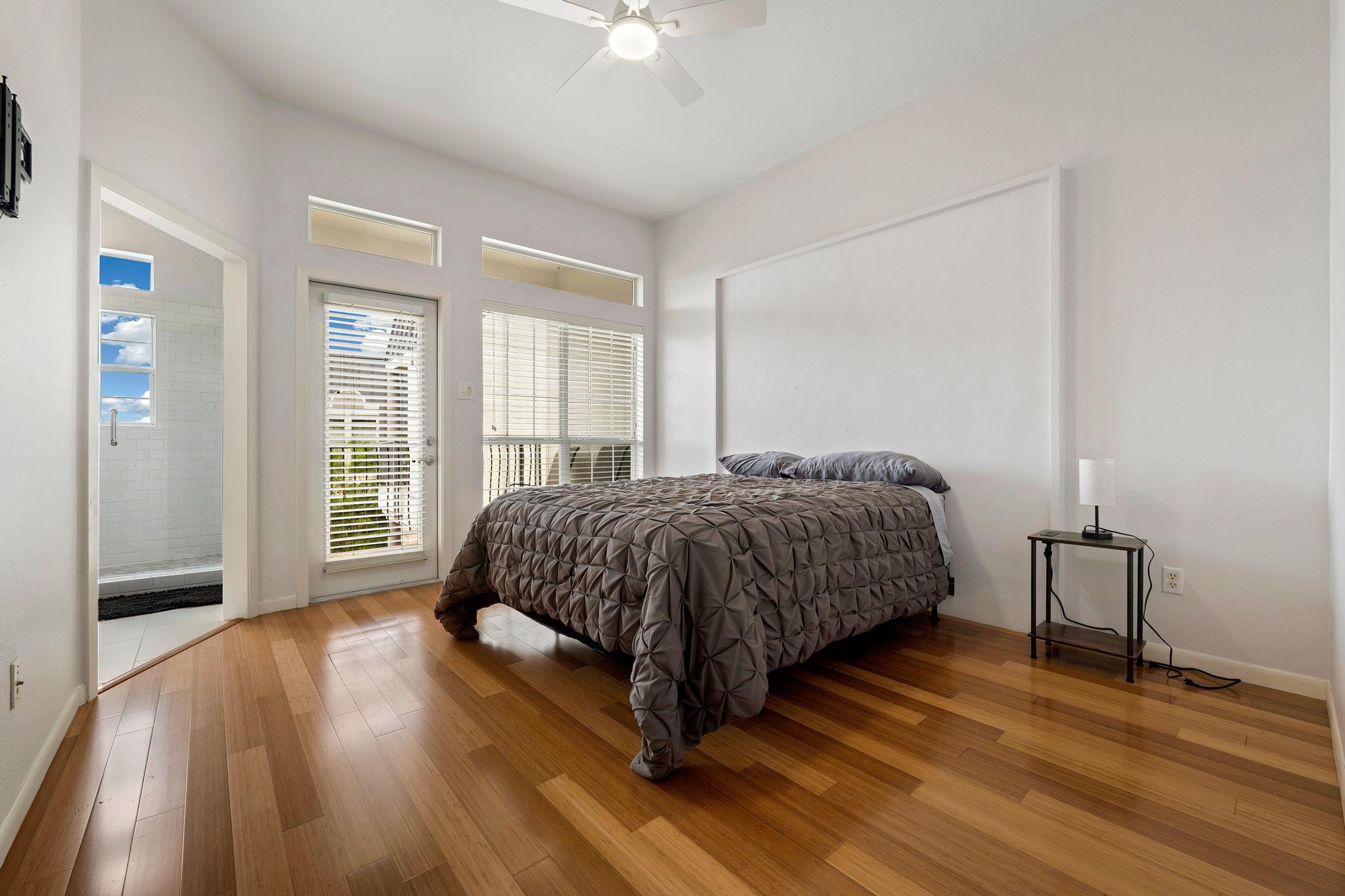 2918 Ranch Road 620, Unit J162 Austin, TX 78734 - Photo 19 of 26 Bedroom featuring wood flooring, a ceiling fan, white walls, and a glass-paneled door opening to an outdoor balcony and with remodeled modern bathroom with double vanities and oversized shower
