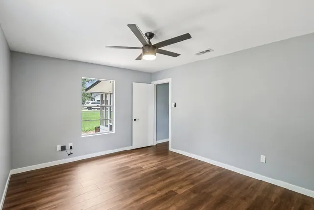 an empty room with wooden floor fan and windows