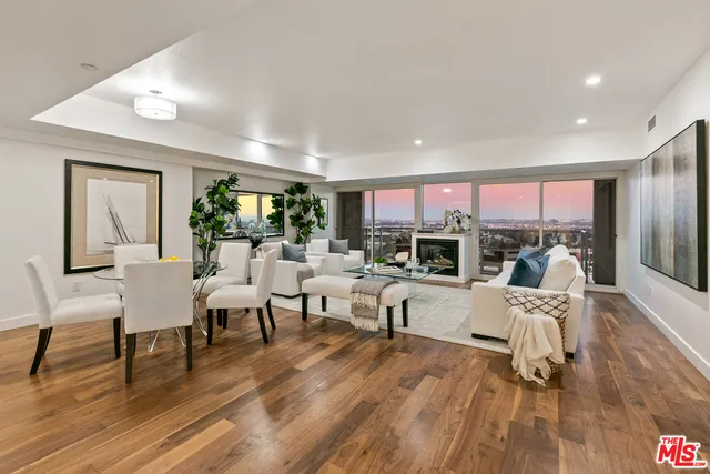 a living room with furniture two large window and wooden floor