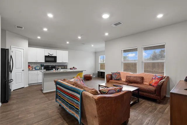 a living room with stainless steel appliances furniture windows and a kitchen view