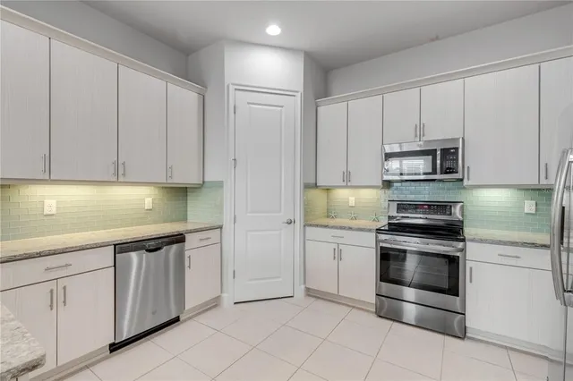 a kitchen with stainless steel appliances granite countertop a refrigerator a stove a sink and white cabinets