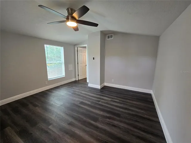 an empty room with wooden floor ceiling fan and window