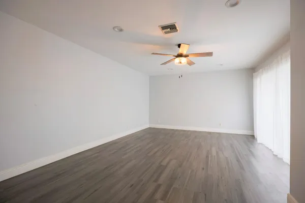 an empty room with wooden floor fan and windows