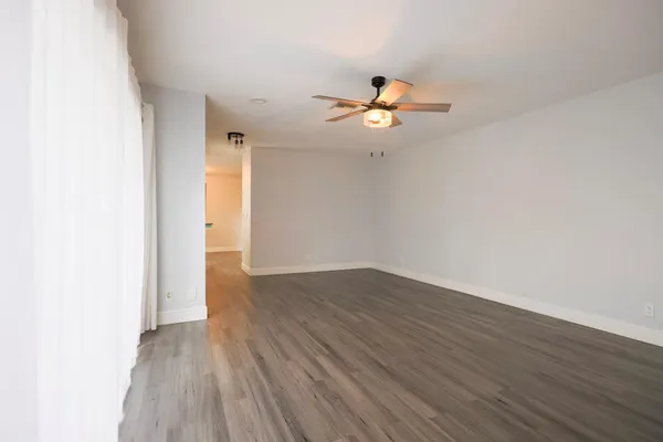 an empty room with wooden floor ceiling fan and windows