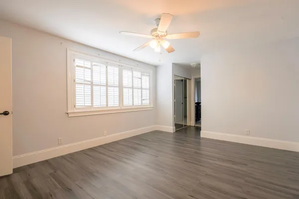 an empty room with wooden floor fan and windows