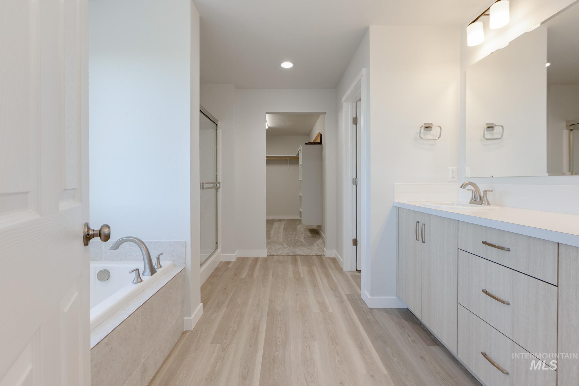 1639 Celina Street Middleton, ID 83644 - Photo 12 of 19 Bathroom featuring a light wood-finish floor, a soaking tub with tile surround, a glass-enclosed shower, a double vanity with light wood-finish cabinetry, and a large mirror with integrated lighting