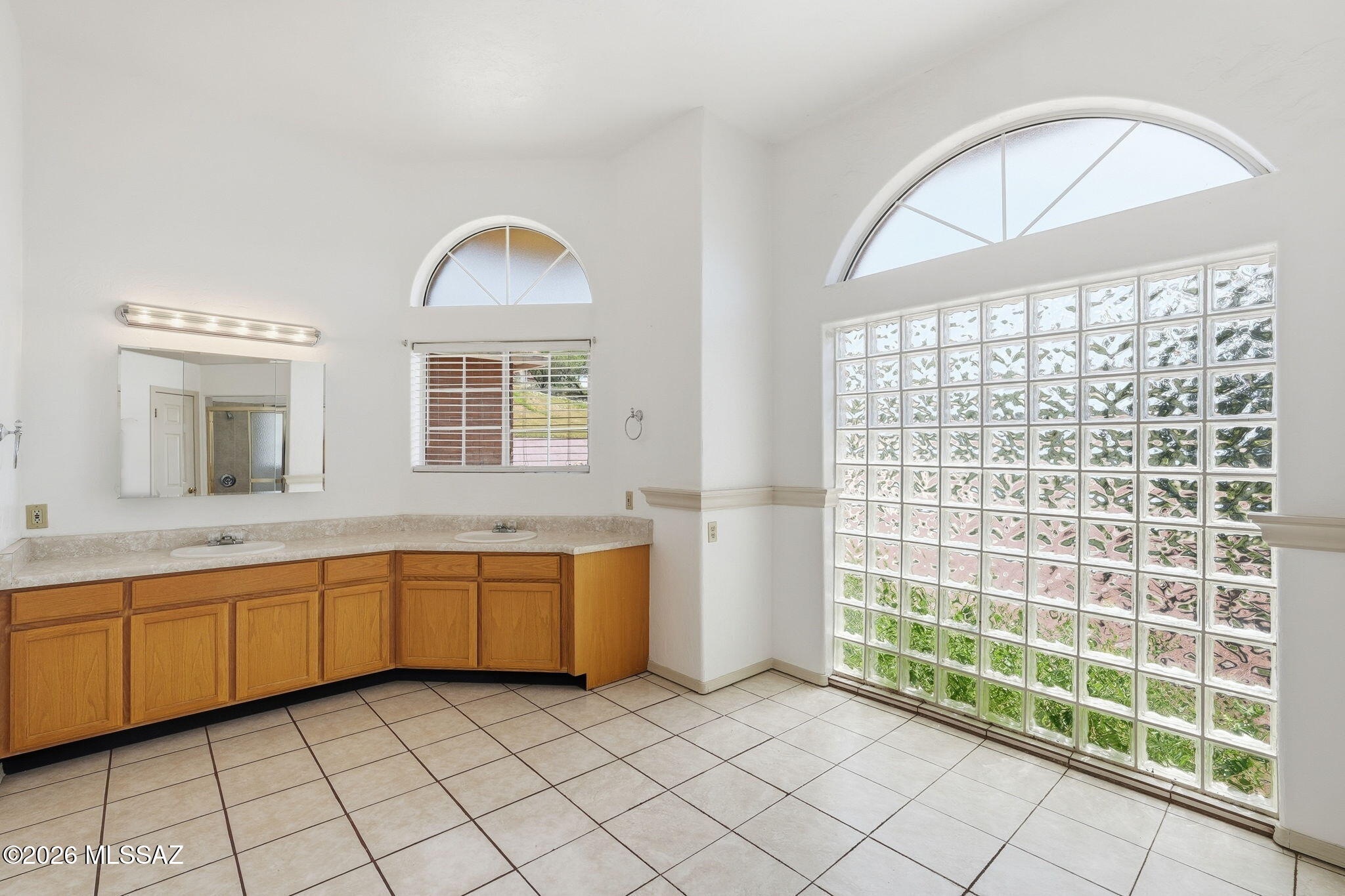 1242 Vista Court Rio Rico, AZ 85648 - Photo 23 of 51 The spacious primary bathroom offers plenty of room to move about comfortably without ever feeling crowded. A large glass-block wall allows natural light to filter into the room while still maintaining privacy and adding architectural interest. The bathroom is already plumbed for a freestanding tub, giving you the opportunity to create a relaxing retreat if desired. A generously sized tiled shower is ready for everything from a quick morning rinse to a long, refreshing shower at the end of the day. With all the open floor space, you definitely won’t have to worry about bumping into one another while getting ready for the day.