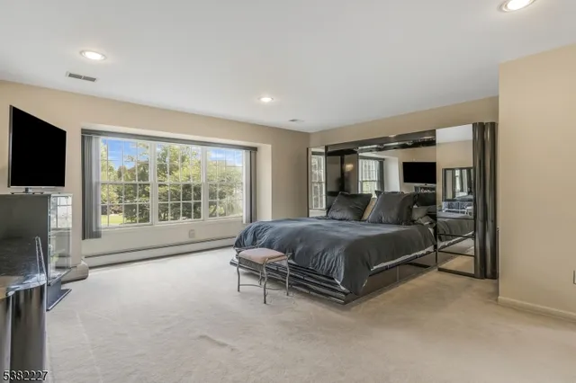 a spacious bedroom with a bed and a flat tv screen on the dresser