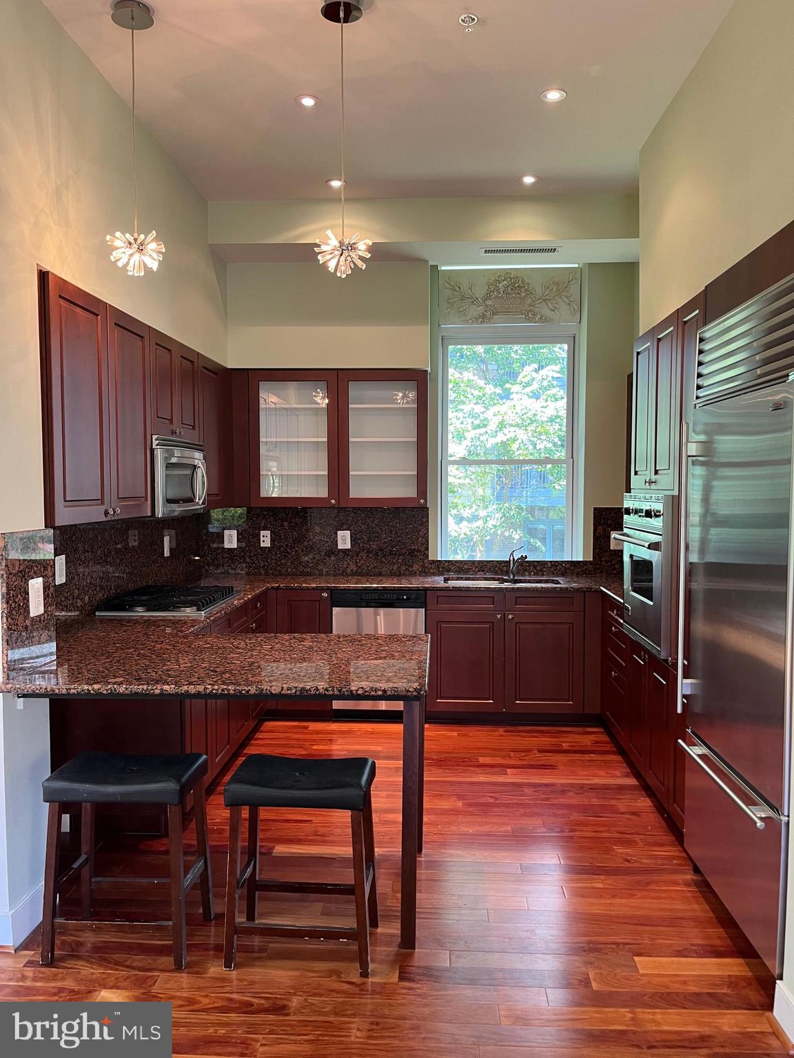 2425 L Street Northwest, Unit 215 Washington, DC 20037 - Photo 14 of 38 a kitchen with granite countertop wooden cabinets dining table and stainless steel appliances
