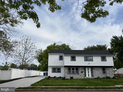 a view of a white house with a small yard and large trees