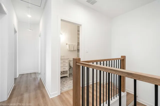 a view of a hallway with wooden floor and a bathroom