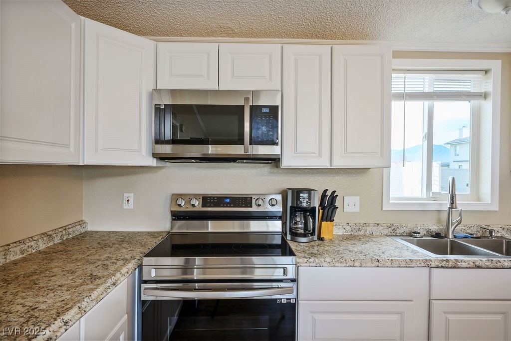 1100 East Gamebird Road Pahrump, NV 89048 - Photo 23 of 37 Kitchen featuring white cabinets, a sink, stainless steel appliances, and a textured ceiling