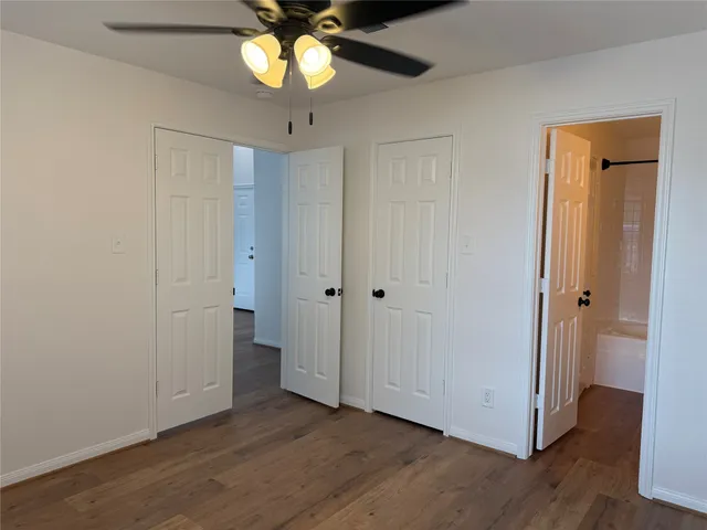 a view of an empty room with wooden floor and a ceiling fan